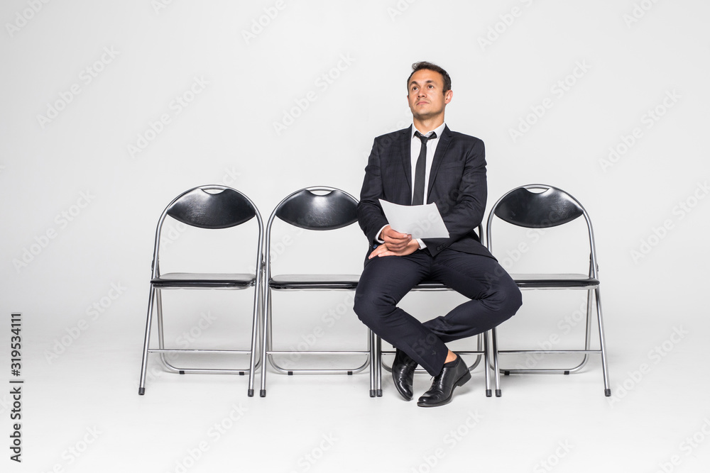 Ready for interview. Thoughtful man in formalwear holding paper while sitting at the chair in waiting room Ready for interview. Thoughtful man in formalwear holding paper while sitting at the chair in waiting room