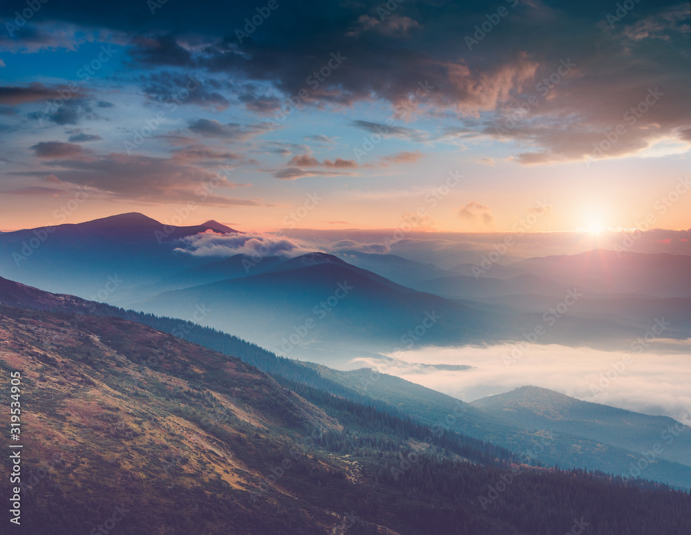 Beautiful landscape of summer mountains at sunrise. Misty slopes of the mountains in the distance. View of morning forest hills in fog and rays of sunlight. Concept of the awakening wildlife. 