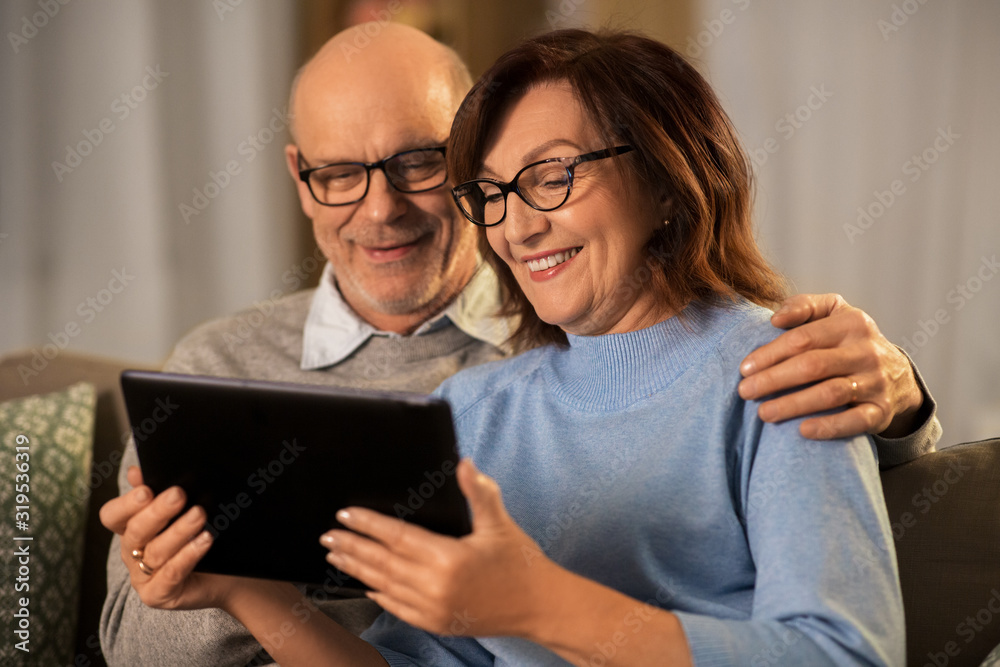 technology, old age and people concept - happy smiling senior couple with tablet pc computer at home in evening technology, old age and people concept - happy smiling senior couple with tablet pc computer at home in evening