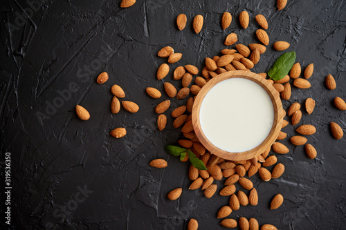 Fresh almond milk in wooden bowl and almonds on black stone background