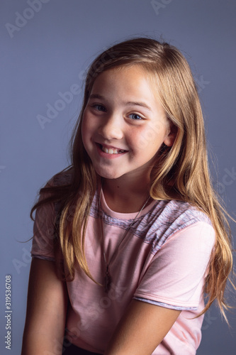 Portrait of a smiling young girl with long blond hair wearing a pink shirt isolated on a blue gray background photo