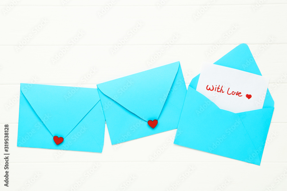 Blue paper envelopes with red hearts and text With Love on white wooden table Blue paper envelopes with red hearts and text With Love on white wooden table