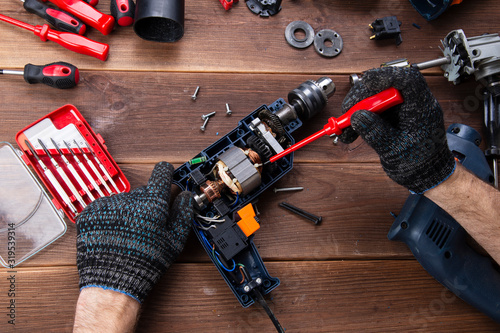 the master repairs a broken electrical device: drill, cutter on a wooden table. Electric Tool Repair Shop