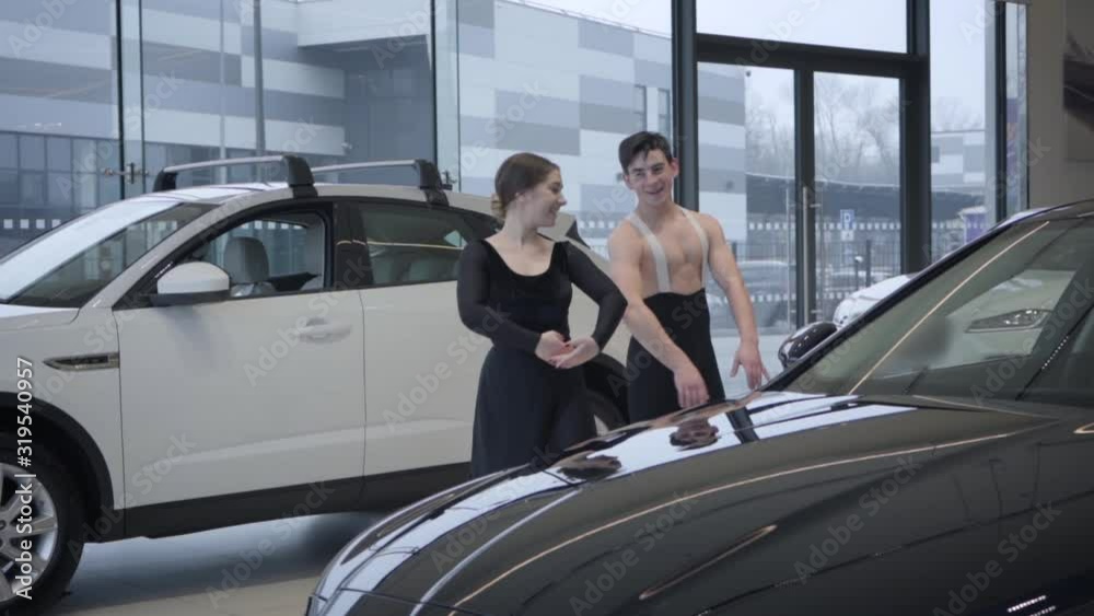 Cheerful Caucasian man and woman dancing ballet in car dealership, slowmo. Male and female ballet dancers moving in auto showroom. Automobile industry, art, elegance. Slow motion. Cheerful Caucasian man and woman dancing ballet in car dealership, slowmo. Male and female ballet dancers moving in auto showroom. Automobile industry, art, elegance. Slow motion.