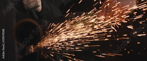 Blacksmith with angle grinder sparks unrecognizable dark close up cinemascope widescreen photo