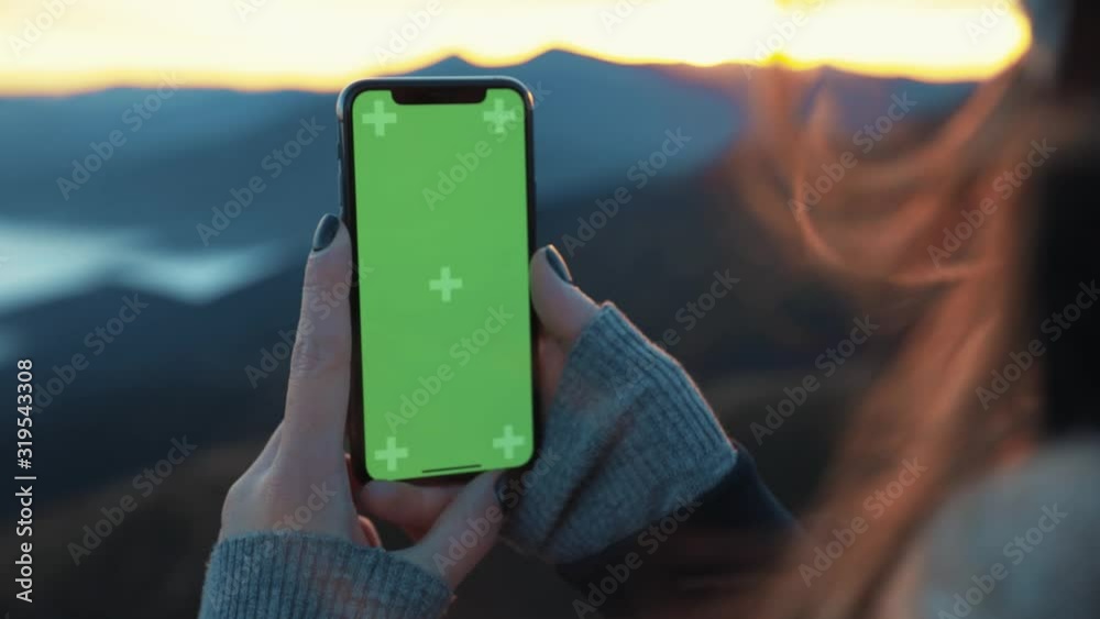 Close up young female hand holding smartphone with green screen chroma key on green grass background mountains outdoors cell text cellphone finger slow motion