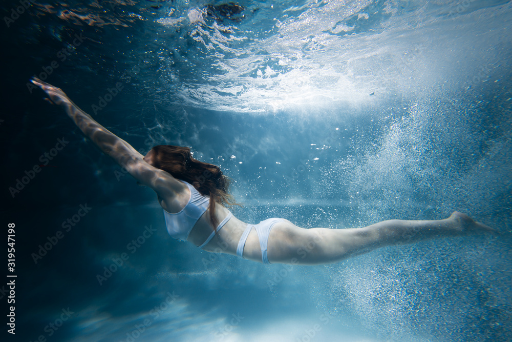 Woman dives under water among the rays of light and air bubbles
