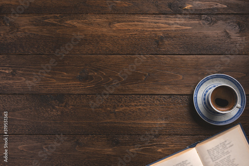 Open book and cup of coffee, on wooden background. Flat lay, top view, copy space.