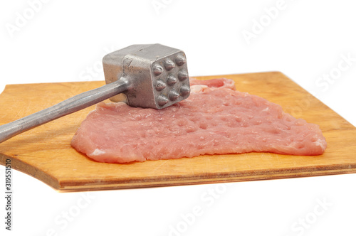 Fresh pork tenderloin with a metal hammer for beating meat on a wooden cutting board.
