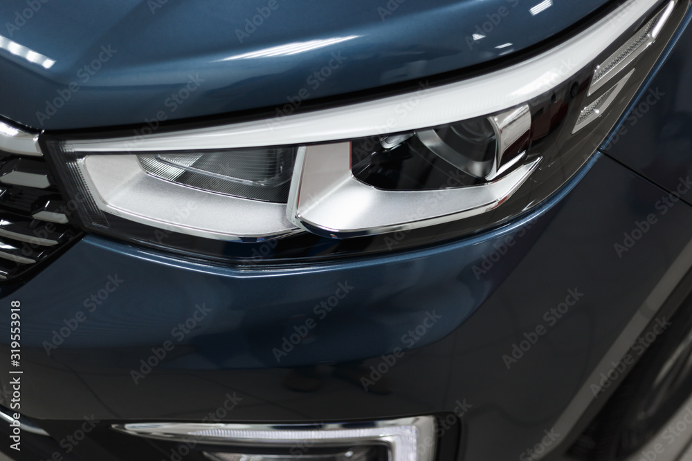Close-up headlights of a modern blue color car. Detail on the front light of a car. Modern and expensive car concept. The car is in the showroom. Automotive concept. Classic blue color