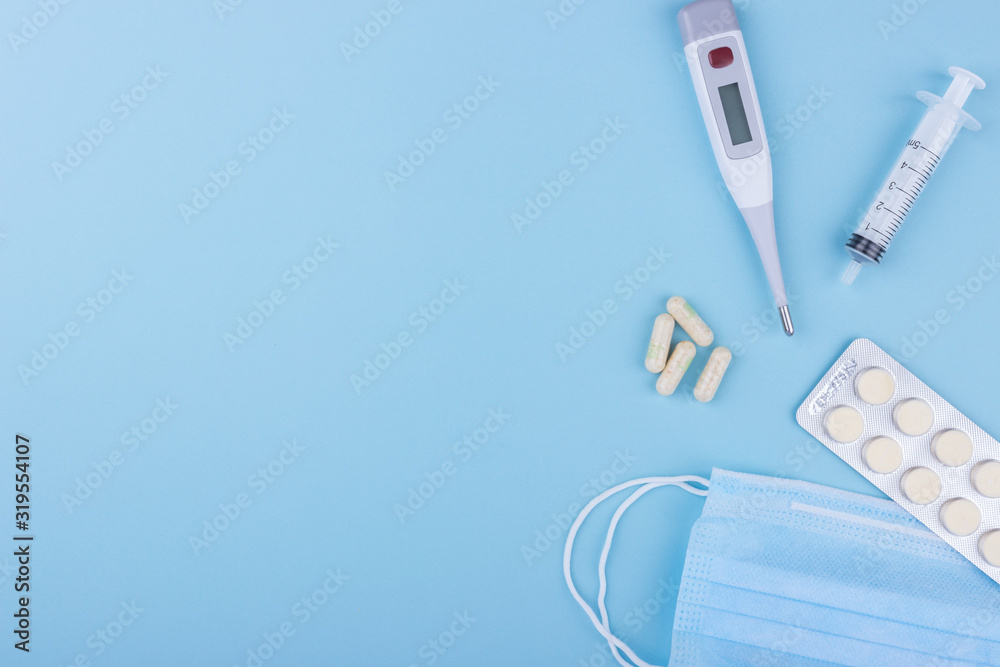 Concept image of four yellow capsule, electronic thermometer, medical mask, syringe on a blue background. Flat lay, copy space. Medicine concept seasonal illness flu, virus, runny nose, temperature. - obrazy, fototapety, plakaty 