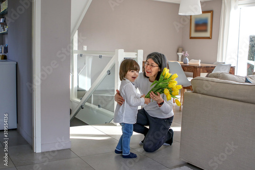 Happy womenâ€™s day. Little boy congratulating his grandmother giving her with bouquet of yellow tulip flowers in her house. Grandparents day. Focus on woman photo
