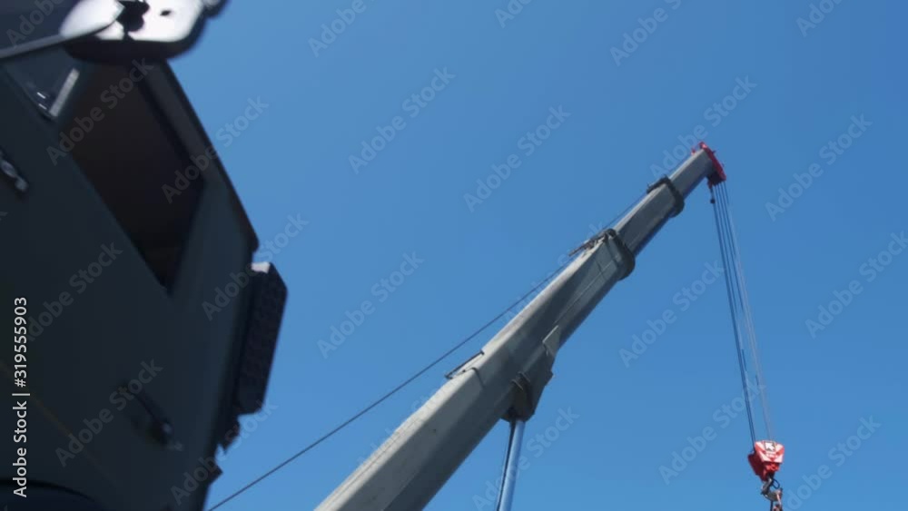 The red hook of a construction crane hanging down from a boom on a clear sky The red hook of a construction crane hanging down from a boom on a clear sky