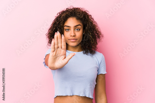 Young african american woman against a pink background standing with outstretched hand showing stop sign, preventing you.