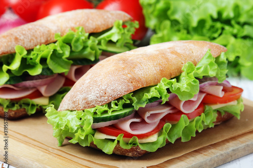 Two sandwiches with fresh vegetables, ham and cheese in ciabatta bread