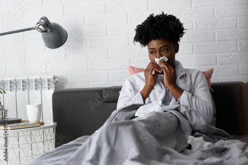 Young African-American woman lying in bed at home. Feeling ill having flu.