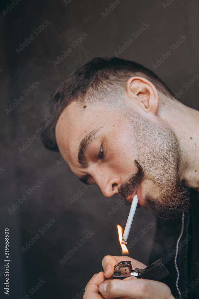 Fototapeta premium portrait of a young stylish bearded man with a cigarette in his hands: not a healthy lifestyle, smoking, bad habits and nicotine addiction