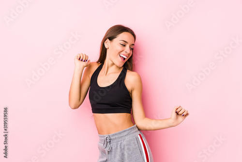 Young caucasian fitness woman posing in a pink background dancing and having fun. © Asier