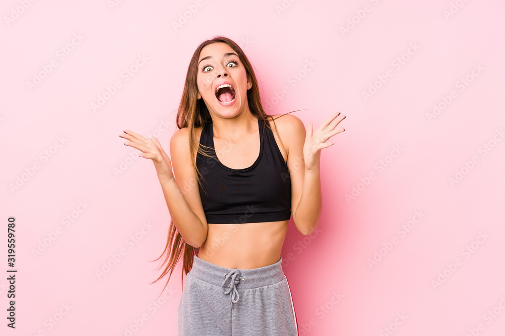 Young caucasian fitness woman posing in a pink background celebrating a victory or success, he is surprised and shocked. Young caucasian fitness woman posing in a pink background celebrating a victory or success, he is surprised and shocked.