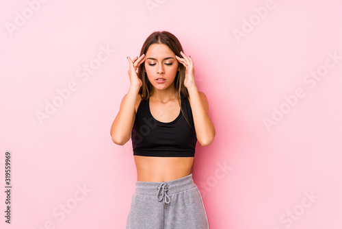 Young caucasian fitness woman posing in a pink background touching temples and having headache.