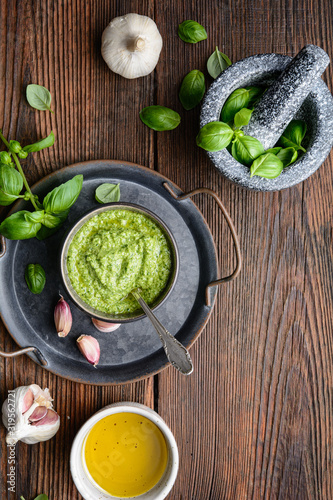 Homemade fresh basil pesto sauce in a bowl, decorated with leaves, garlic and mortar with copy space