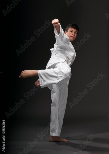 a teenager dressed in martial arts clothing poses on a dark gray background, a sports concept