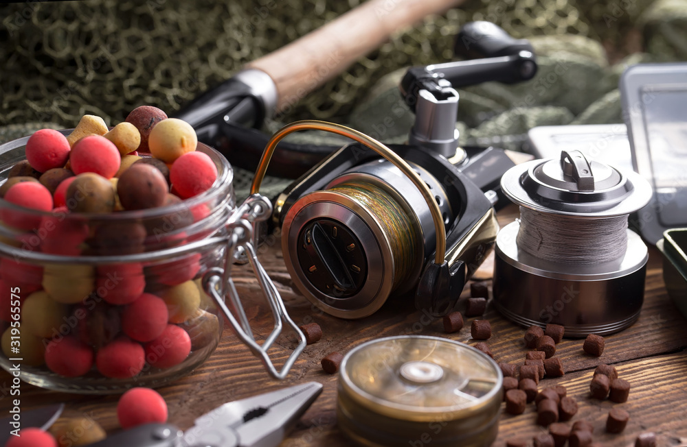 Fototapeta premium Fishing rods and spinnings in the composition with accessories for fishing on the old background on the table