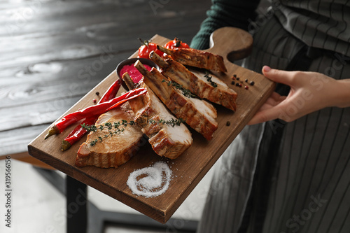 Woman holding serving board with delicious roasted ribs, closeup