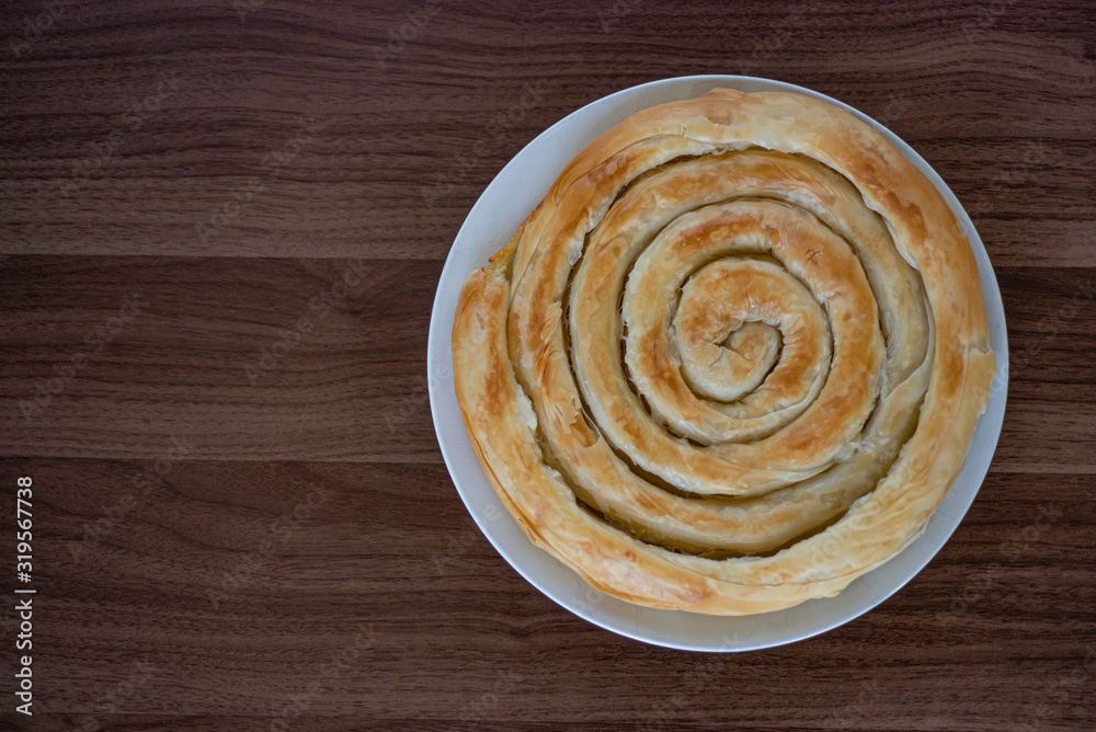 Spiral-shaped Greek Cheese pie (Kichi Kozanis) on brown wood surface, close up view. Warm cheese filling and so crispy pastry. Free copy space. Top or above view. Spiral-shaped Greek Cheese pie (Kichi Kozanis) on brown wood surface, close up view. Warm cheese filling and so crispy pastry. Free copy space. Top or above view.
