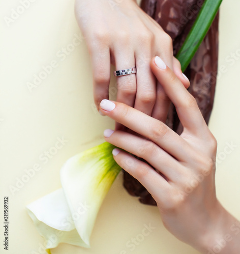pretty perfect woman hands with white manicure and big flower on colorful yellow background, spa concept