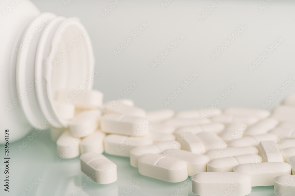 White medicine tablets spilled on table from pill bottle. Medications drugs or supplements or opioid addiction from pain killers, macro with selective focus.