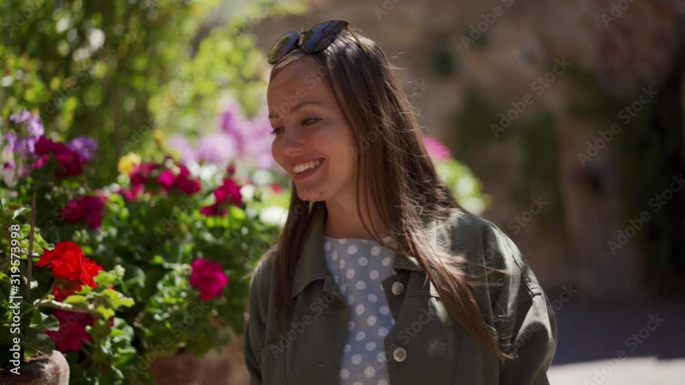 Smiling girl with sunglasses in jacket walks along flower bed, touches flowers Smiling girl with sunglasses in jacket walks along flower bed, touches flowers