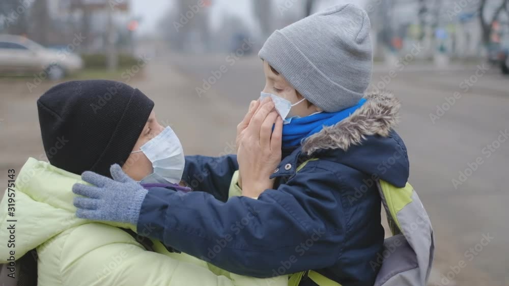 Protection against Chinese coronavirus in a European city. Mom corrects a protective medical mask to a little son on the street.
