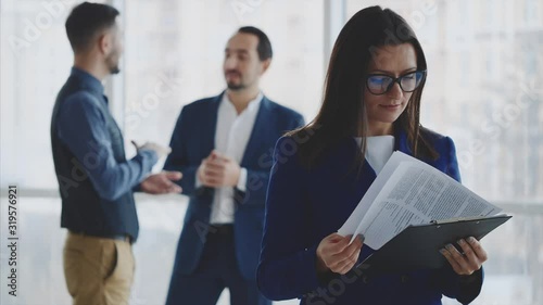 Male business workers are discussing issue on the light blurred background. Woman is turning over pages on the forefront. She is wearing glasses. Copy space. Close up. 4K.