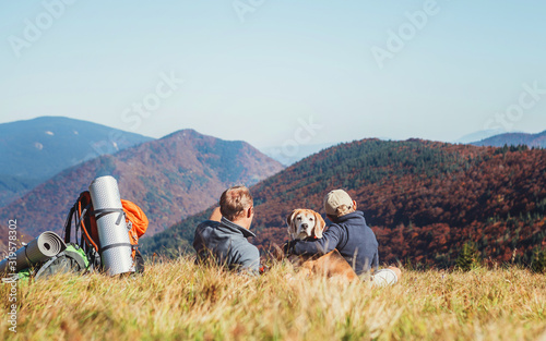 Father and son backpackers hikers resting on mountain hill and enjoying Low Tatras landscape with their beagle dog. Mountain hiking with kids and pets concept image.