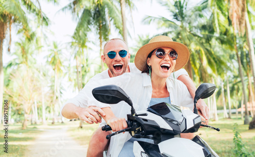 Smiling in love couple travelers riding motorbike under palm trees in their island vacation