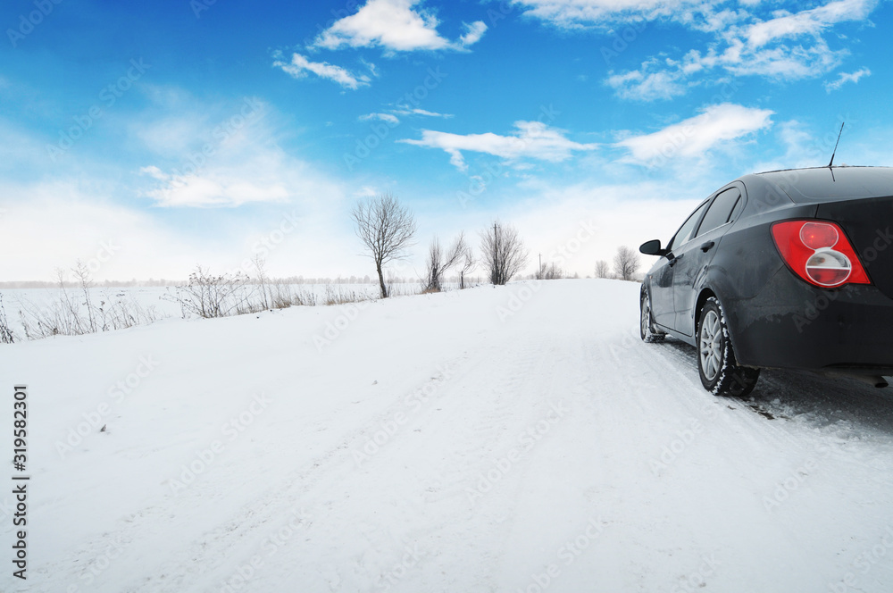 Car on the winter countryside road with snow against a sky with clouds