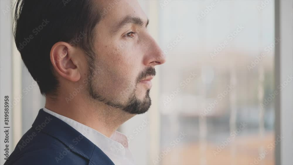 Businessman in formal suite stands in front of panoramic window with city view. Serious man. Profile view. Outboard profile. Close up. Animation. 4K. Businessman in formal suite stands in front of panoramic window with city view. Serious man. Profile view. Outboard profile. Close up. Animation. 4K.