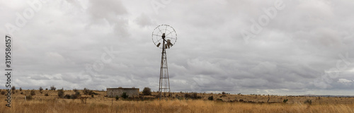typical farming scene of an old tin wind powered water pump standing tall in an open field full of dry, drought affected grassland, on a cloudy overcast day near Melbourne, Victoria, Australia