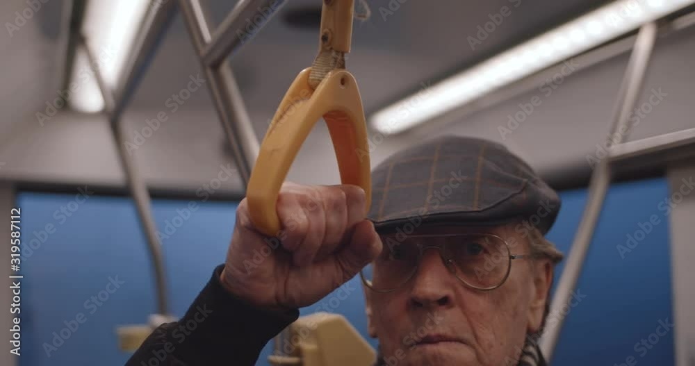 Close up of the old Caucasian smiled man in glasses and gat coming in the tram or bus in the evening and holding a handle.