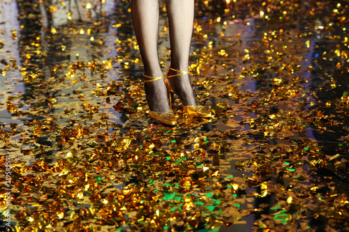 Fototapeta Naklejka Na Ścianę i Meble -  Women's legs in fishnet tights in gold shoes on a gold floor from confetti
