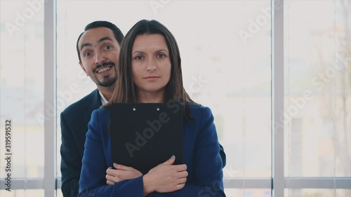 Calm businesswoman is holding forder. Happy cheerful worker is dancing smiling and making faces behind her, on blurred light background. Close up. Animation. 4K. photo