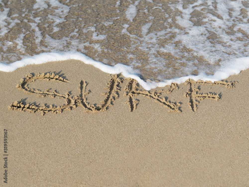 Fototapeta premium Sandy beach with wave and the written in sand word Surf.