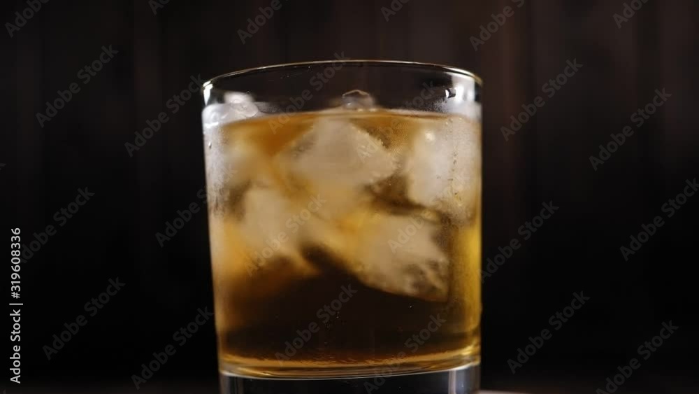 Close-up of a misted glass of chilled single malt whiskey and ice spinning around on a black background. Macro shot. Slow motion.