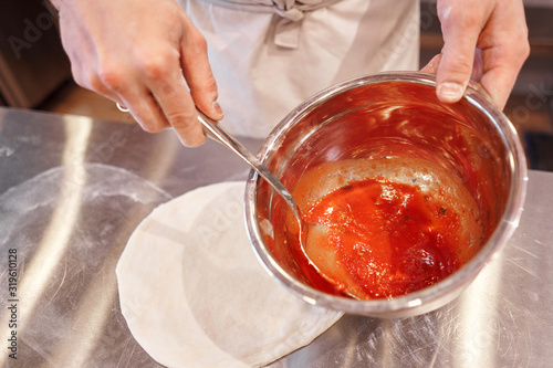 Cooking pizza. the workpiece poured tomato sauce. Closeup hand of chef. Baker in uniform and white apron cooking at kitchen