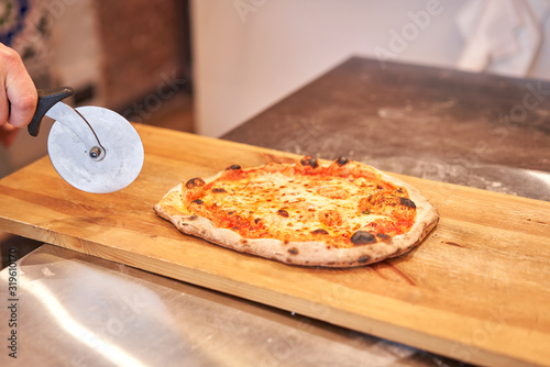 Italian kitchen and cooking concept. Chief with a pizza cutter cutting pizza to pieces at Neapolitan pizzeria. photo