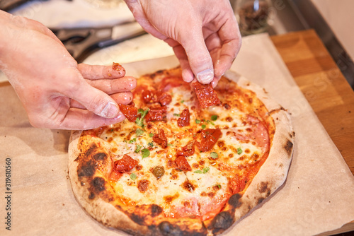 Chief adds ingredients on pizza to pieces at Neapolitan pizzeria. Italian kitchen and cooking concept. photo