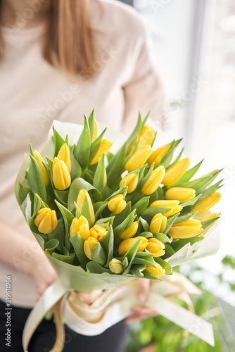 Young beautiful woman holding a spring bouquet of yellow tulips in her hand. Bunch of fresh cut spring flowers in female hands