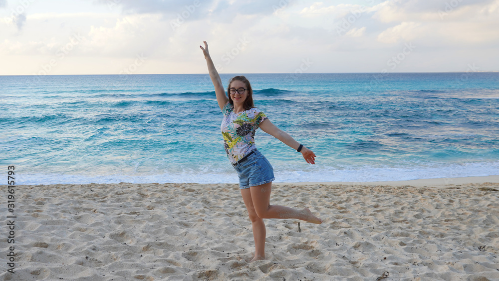 young girl in denim shorts on a sandy beach near the ocean. brunette walks on a background of blue clear water of the Pacific Ocean.