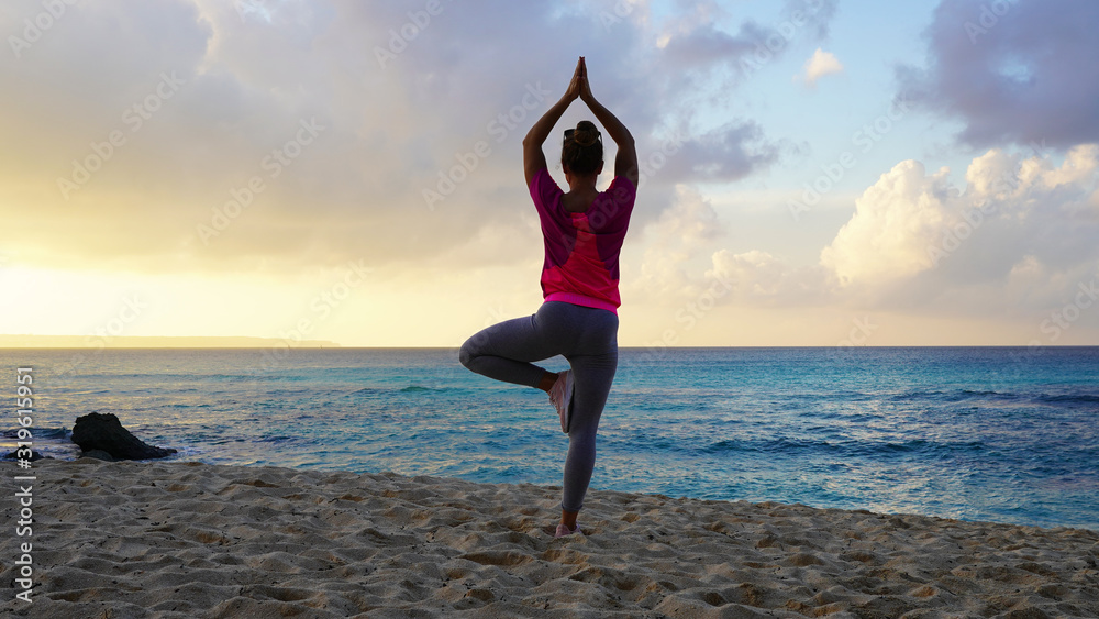 girl do yoga near the ocean while watching the sunset. yoga assans on a tropical beach against a bright orange sunset sky. harmony with nature. sports figure